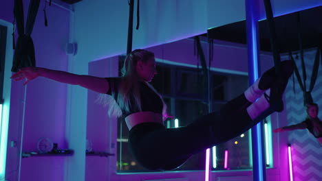 A-woman-does-sports-yoga-in-the-air-on-a-hammock-in-neon-light-performing-graceful-exercises-and-movements-from-stretching-and-dancing-in-slow-motion.
